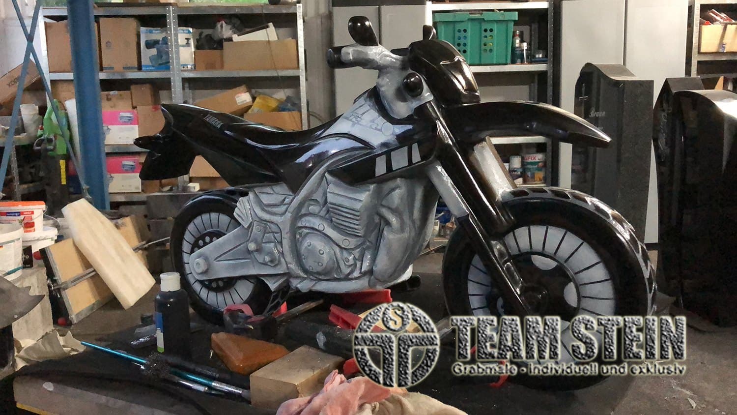 Motorrad aus dunklem Stein in der Werkstatt, im Hintergrund Regale