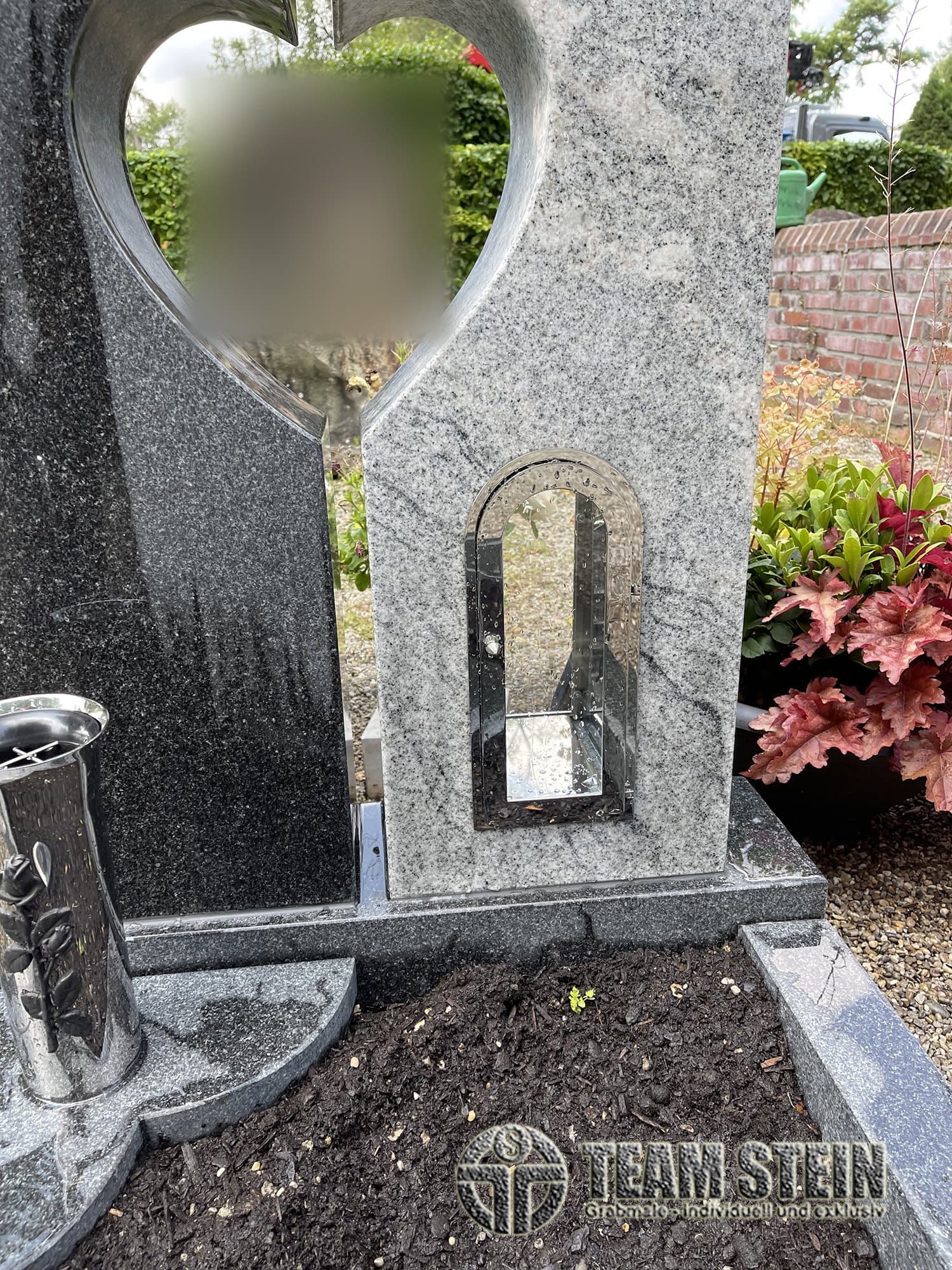 Grabmal aus hellem und dunklem Granit mit Herz-Ausschnitt, Laterne in einer Nische im Stein und Vase