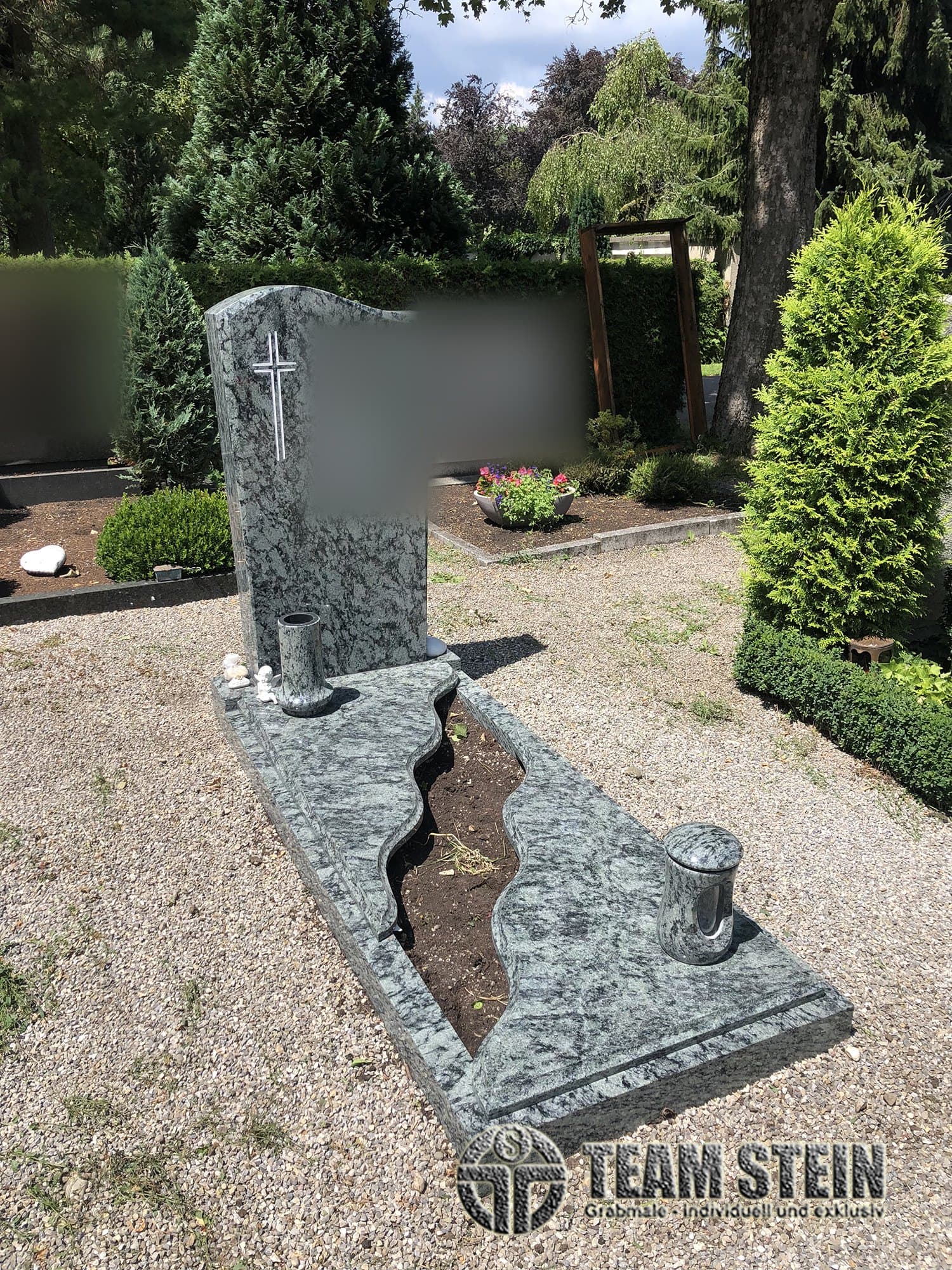 Grabstein aus grünlich-grauem Granit mit Kreuz, Einfassung mit gewellter Pflanzfläche, Vase und Laterne