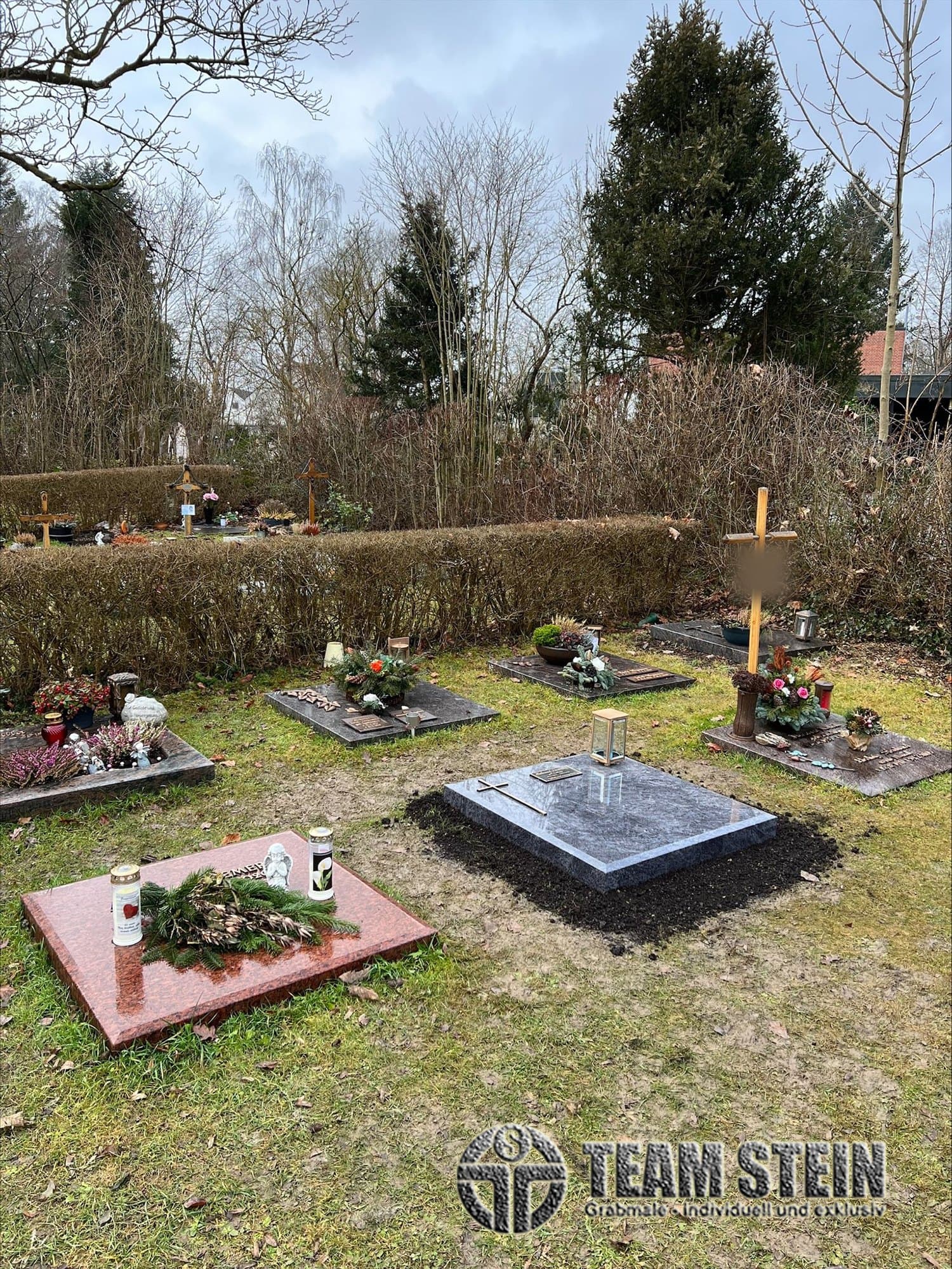 Liegende Grabplatten in einer Wiese, in der Mitte eine dunkle Platte mit Kreuz und Laterne